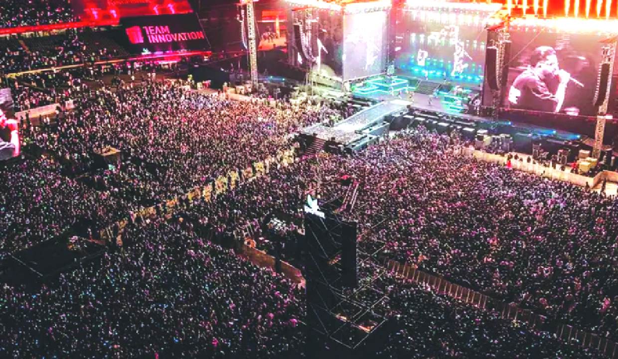 Massive crowd at Karan Aujla concert with people cheering and phone lights creating a sea of lights
